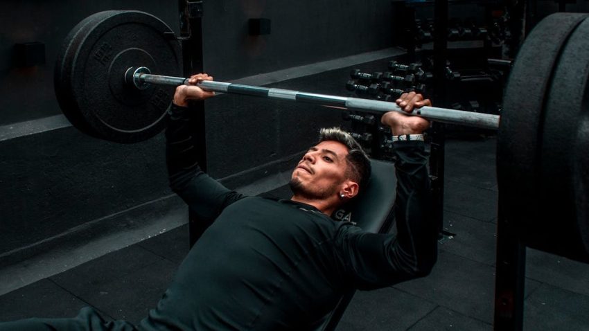 Man performing bench press with heavy barbell in a gym setting, focusing on strength training.